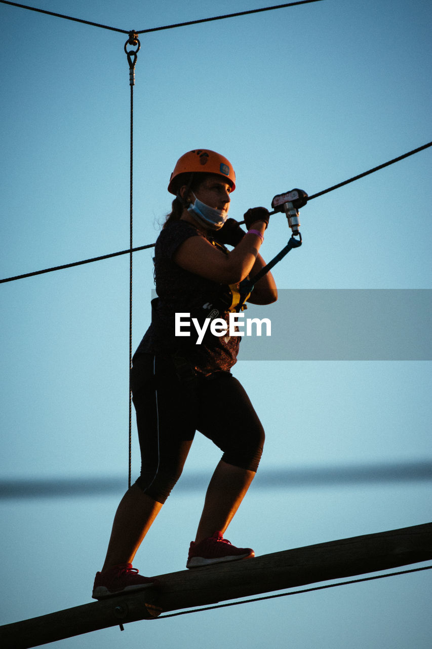 Low angle view of girl hanging on cable against sky