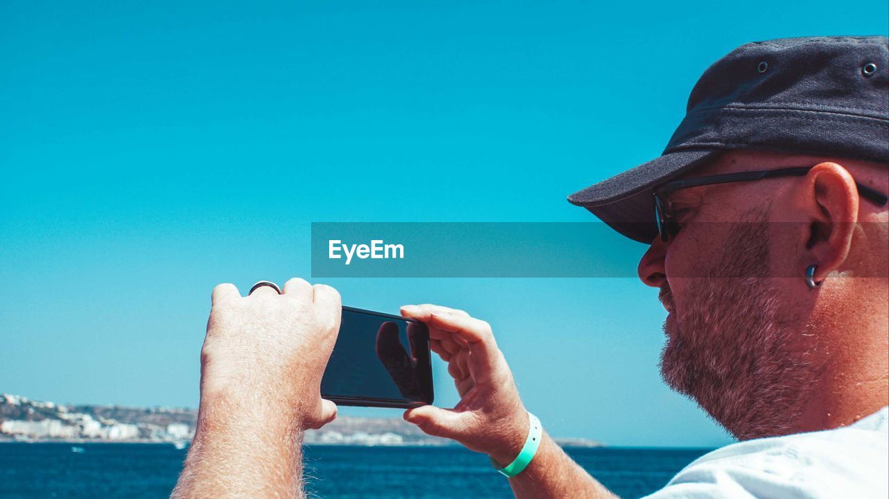 Close-up of man photographing by sea against sky