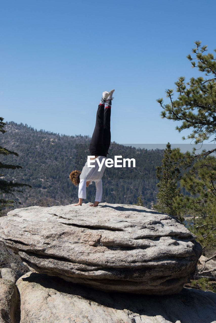 Woman doing handstand on rock against clear sky