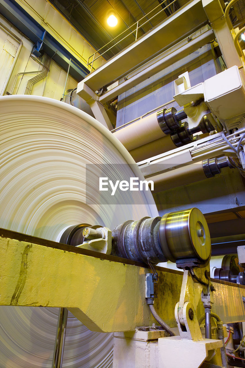 Big rolls of paper coming out of the machinery in a paper mill plant.