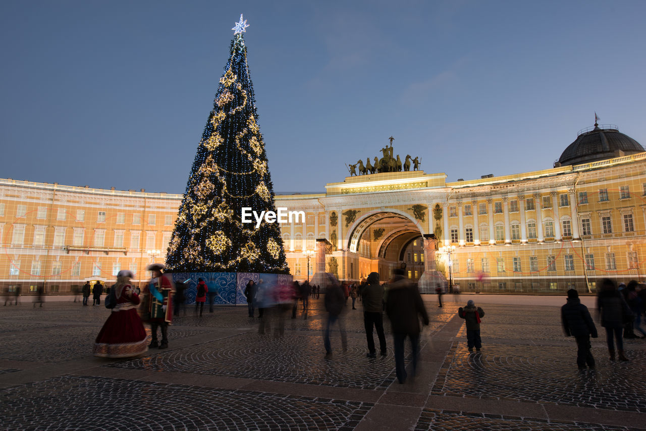 architecture, christmas tree, landmark, travel destinations, built structure, building exterior, city, tourism, travel, holiday, town square, group of people, sky, plaza, crowd, large group of people, christmas, history, the past, illuminated, nature, evening, building, night, tourist, christmas lights, city life, trip, celebration, vacation, tower, christmas decoration, outdoors, decoration, adult, cityscape, women, street, palace, men, tree, lifestyles