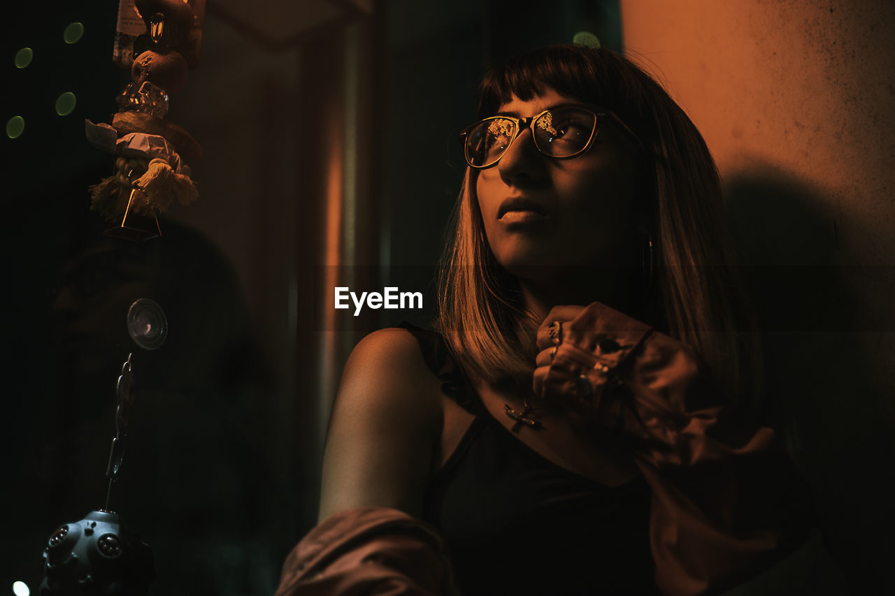 Low angle view of thoughtful young woman looking away while sitting against wall in darkroom