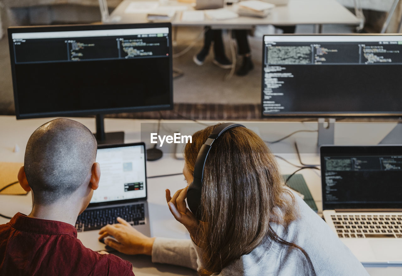 High angle view of female and male hackers coding over laptop in office