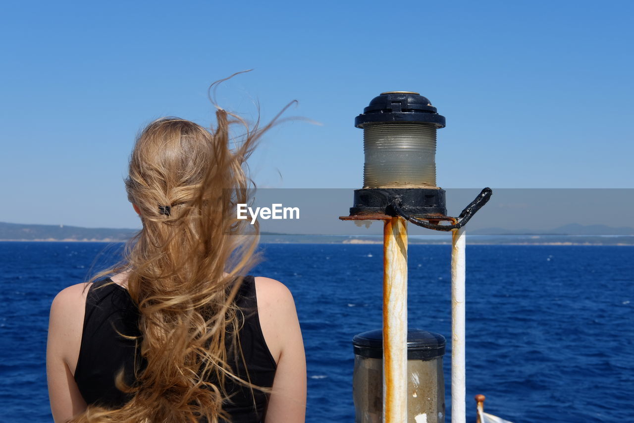 REAR VIEW OF WOMAN LOOKING AT SEA AGAINST BLUE SKY