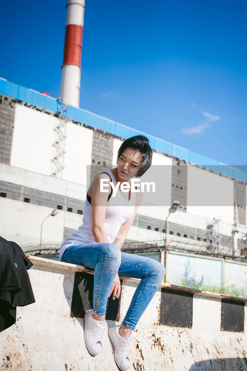 Young woman sitting on barricade against factory