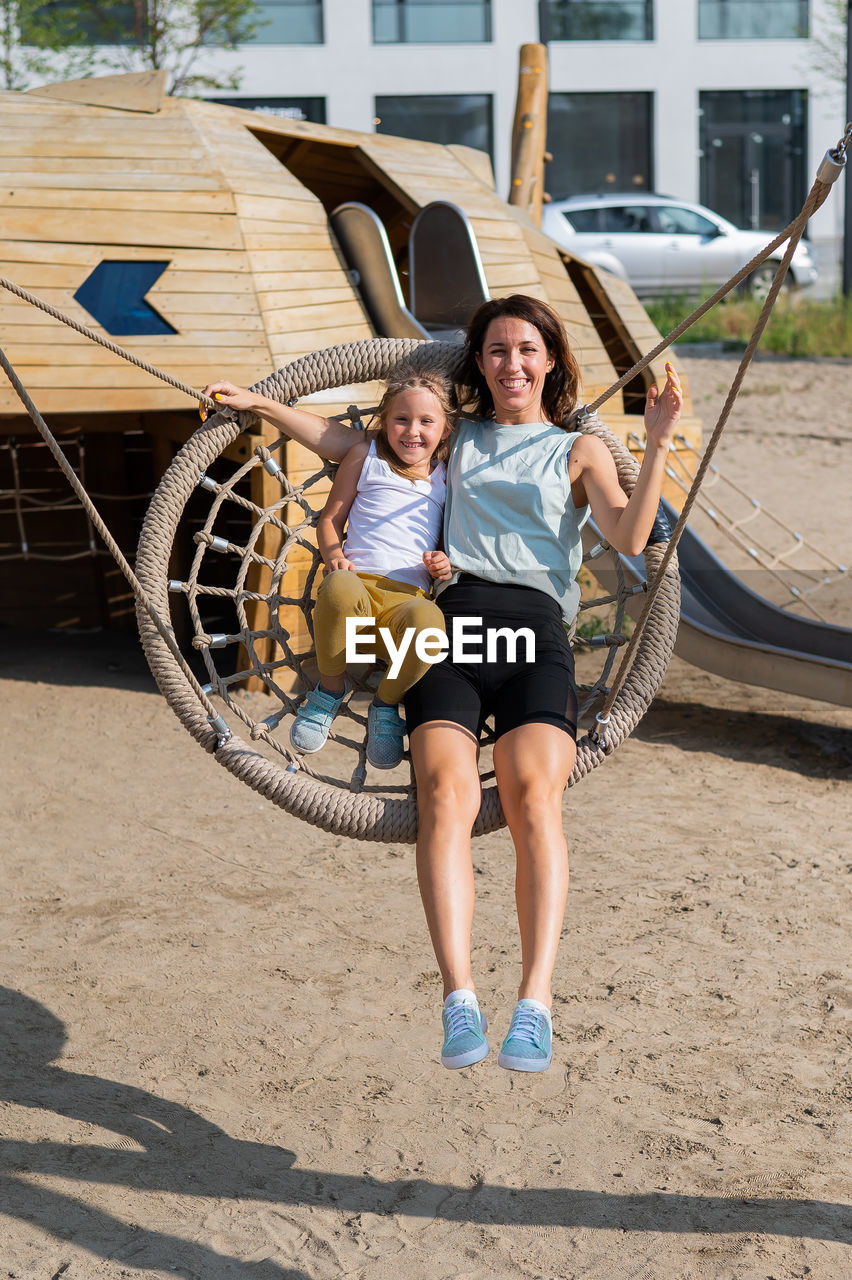 Mom and daughter swing on a round swing. caucasian woman and little girl have fun on the playground.