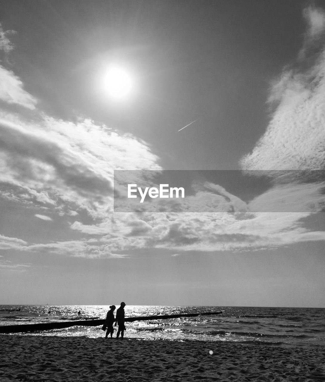 Silhouette man and woman at sea shore against sky