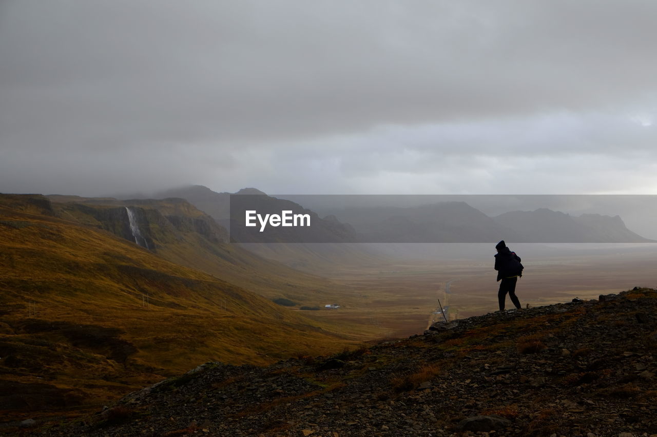 Person hiking on mountain against cloudy sky