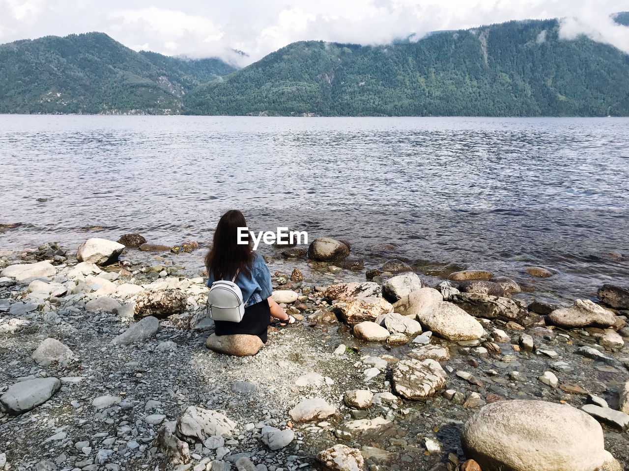 REAR VIEW OF WOMAN SITTING ON ROCK IN WATER