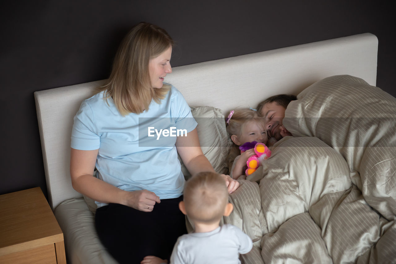 High angle view of parents with children sitting on bed at home