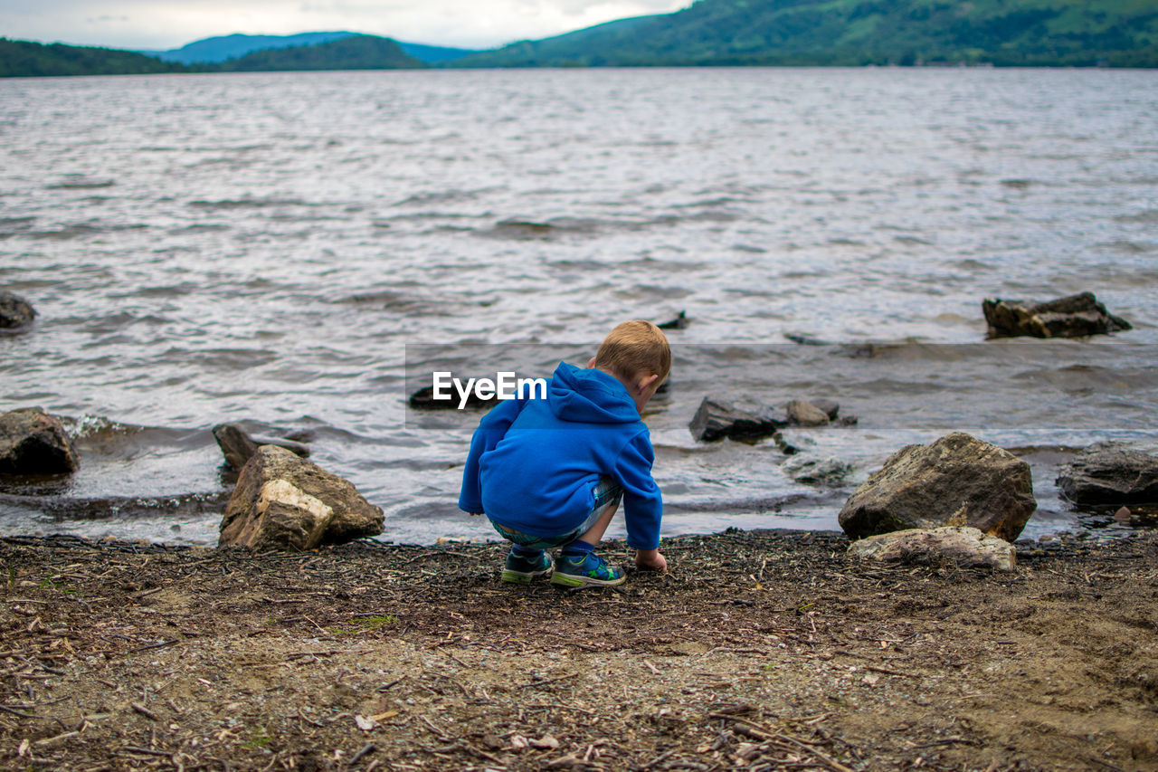 Rear view of boy crouching at riverbank