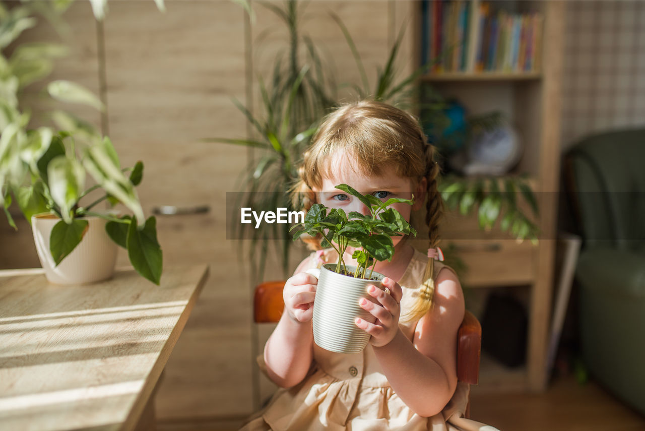 Cute girl holding plant at home