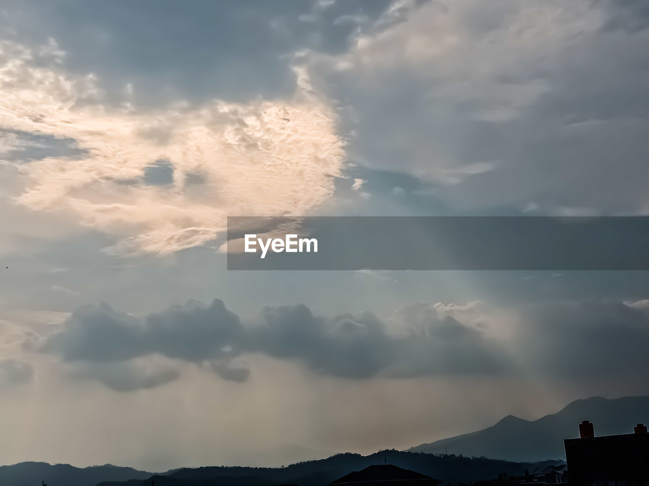 LOW ANGLE VIEW OF SUNLIGHT STREAMING THROUGH SILHOUETTE CLOUDS