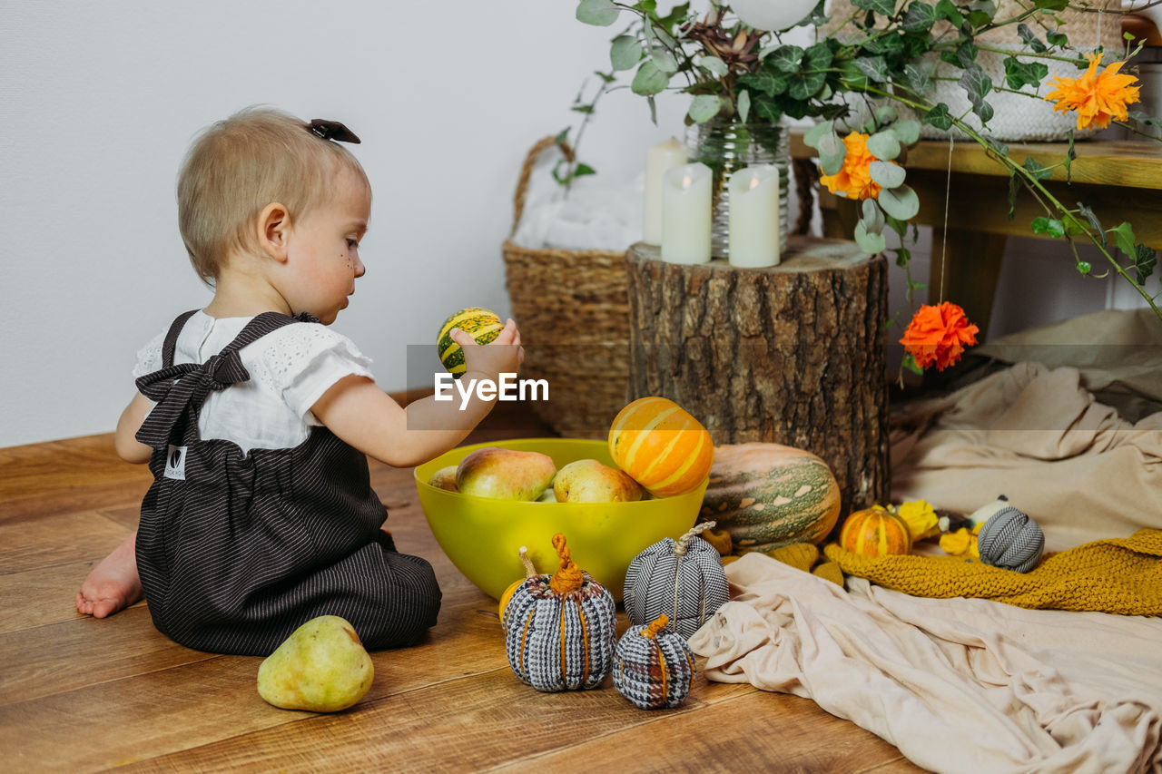 Full length of cute baby holding fruits while sitting at home