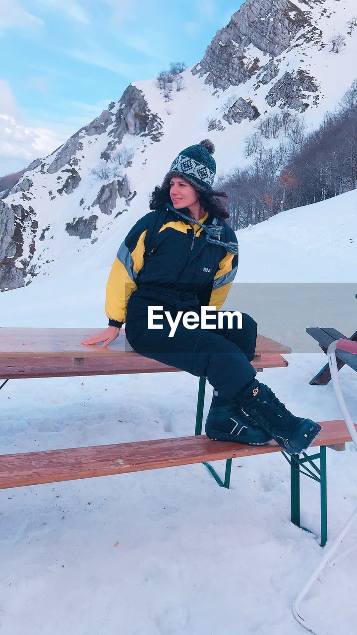 Woman sitting on bench at snowcapped mountain