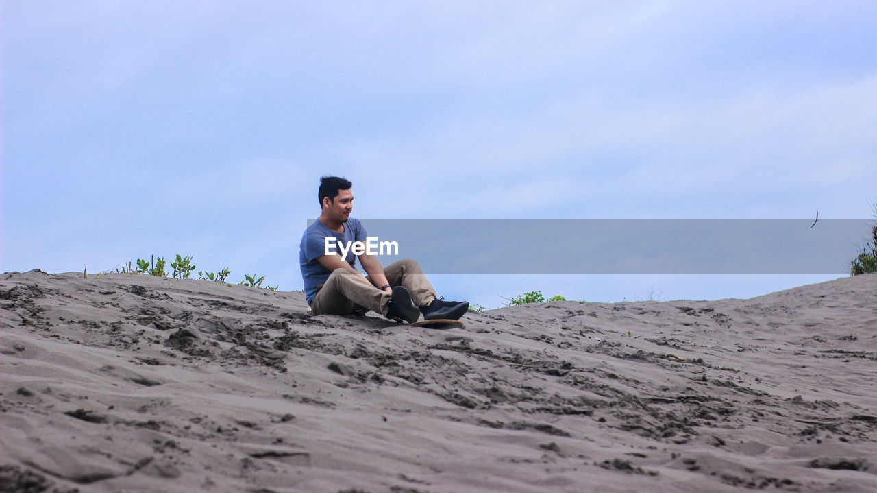 Full length of man sitting on field against sky