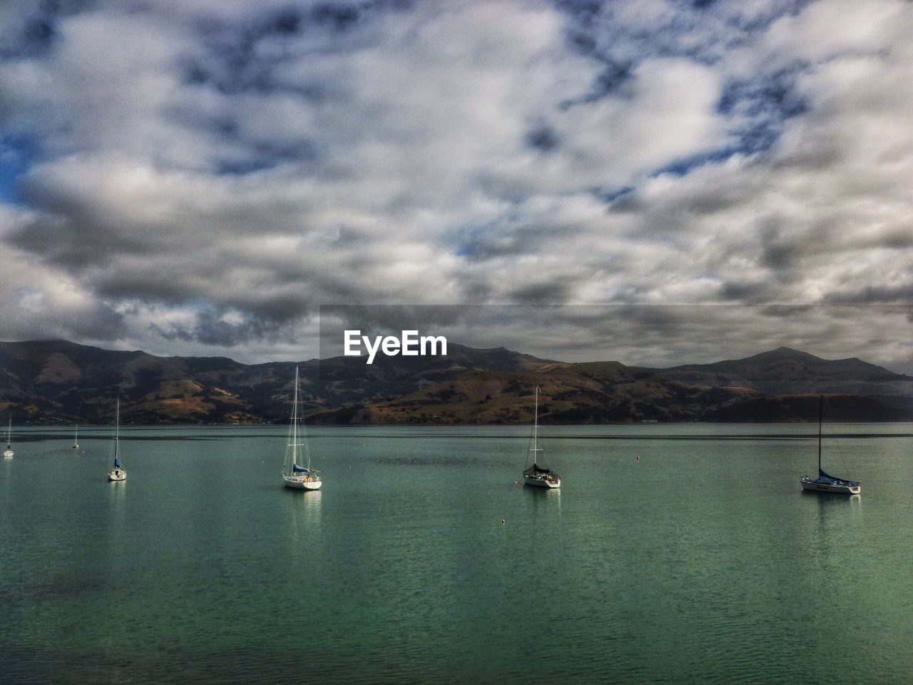 Boats sailing in sea against cloudy sky