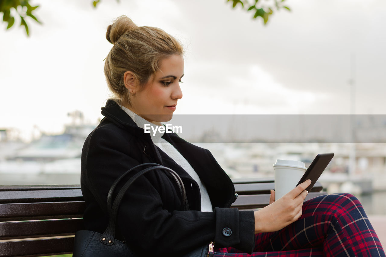 Young woman reads in her electronic book sitting on a bench