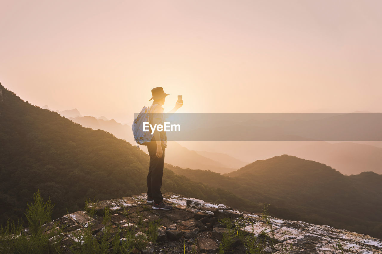 Man standing on rock against sky during sunset