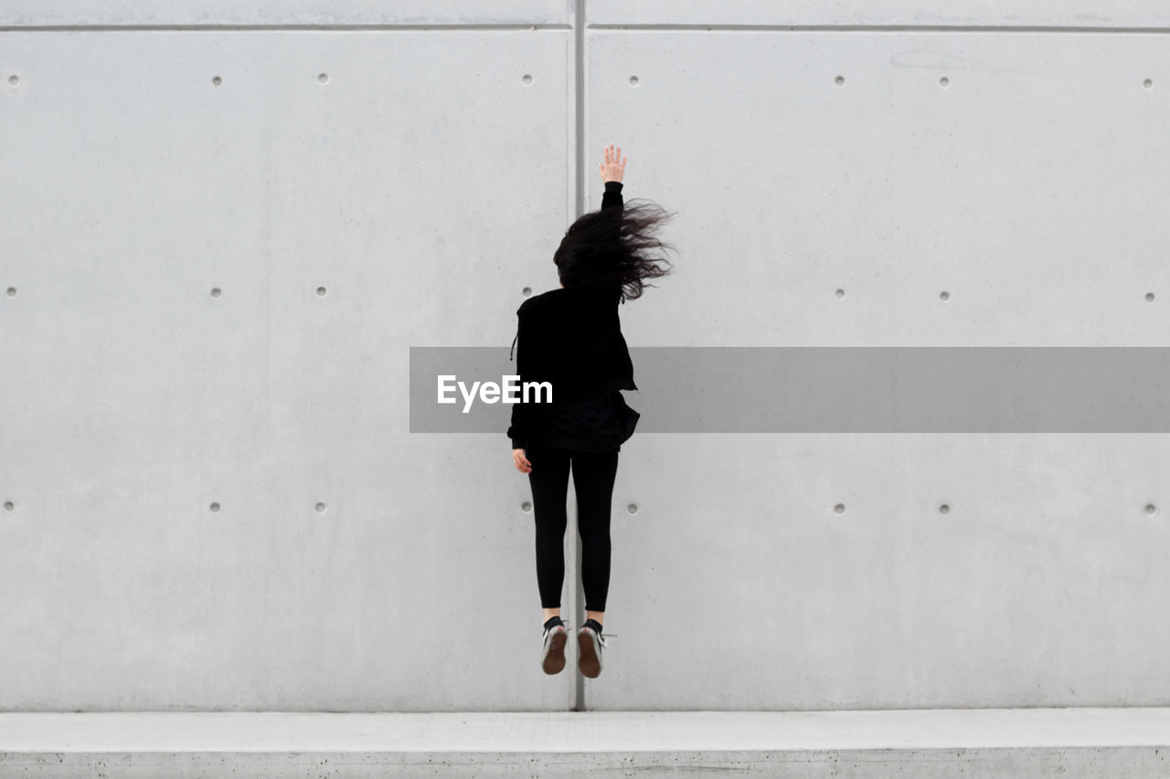 Full length of woman jumping against wall