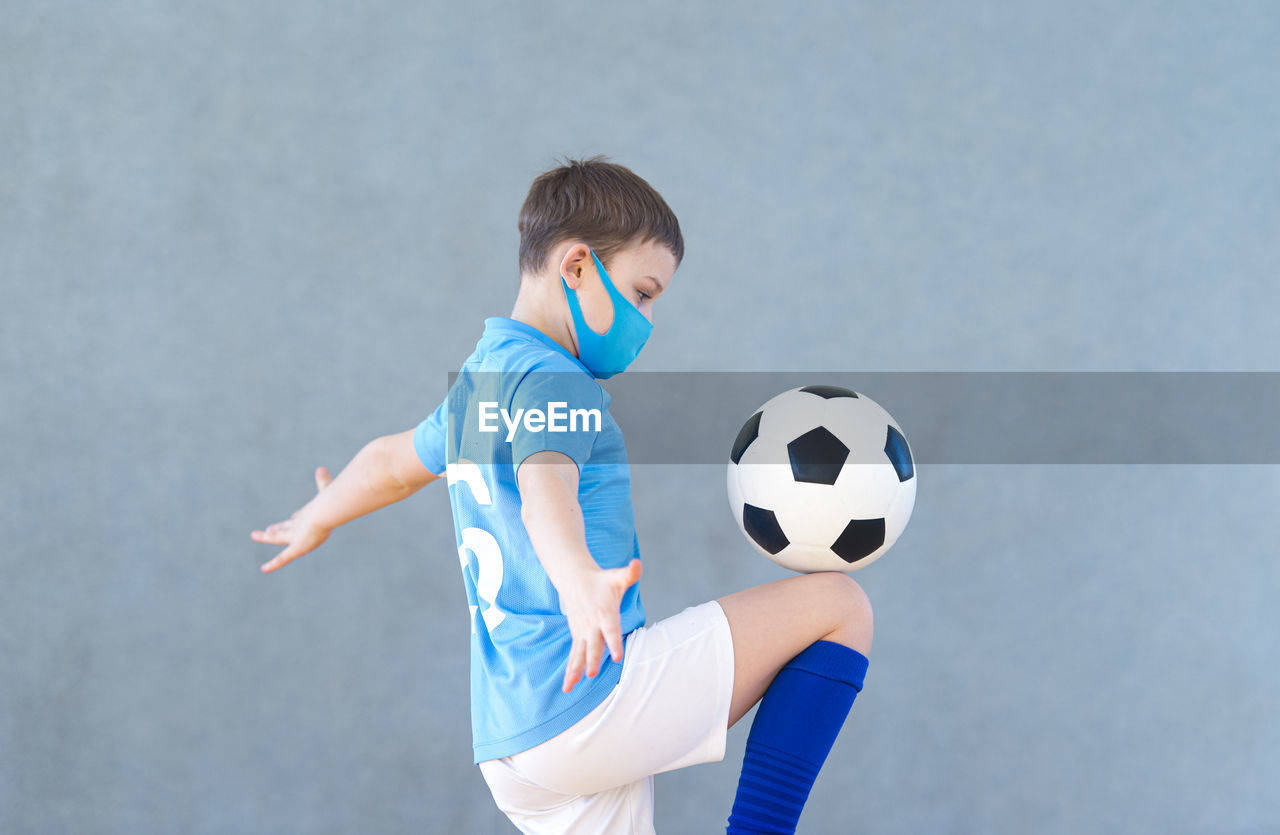 Side view of boy wearing mask playing with soccer ball