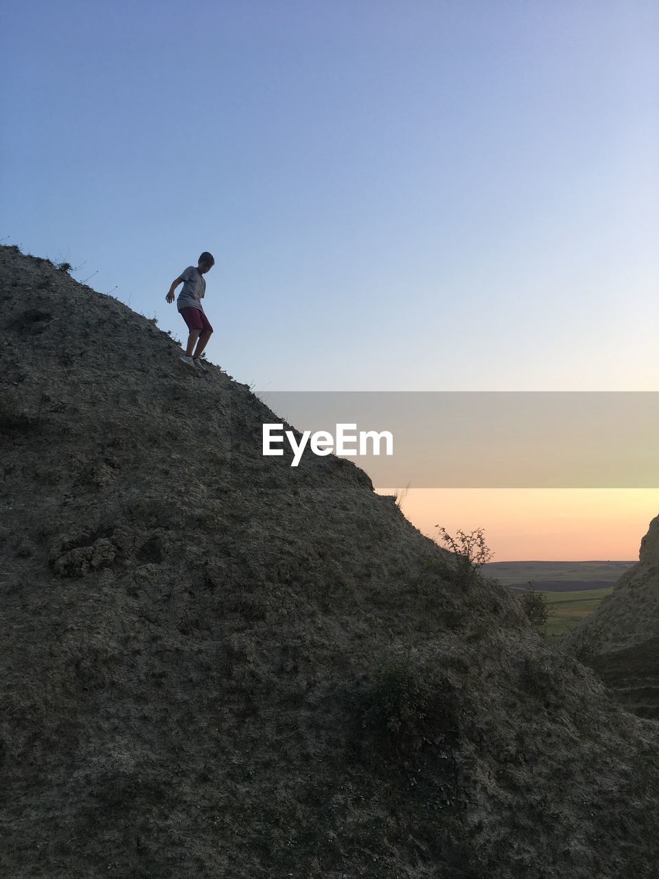 Low angle view of teenage boy standing on hill against sky during sunset