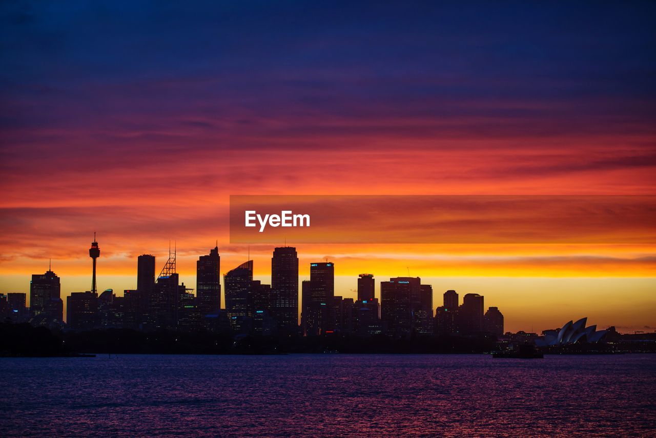 Silhouette of city at waterfront during sunset