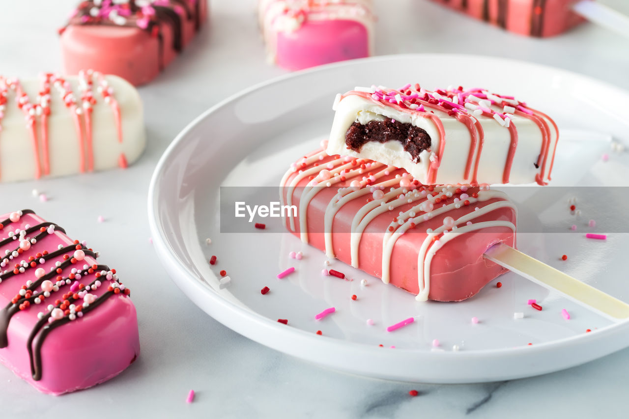 Valentine's day cakesicles on a plate with sprinkles with a bite out of one.