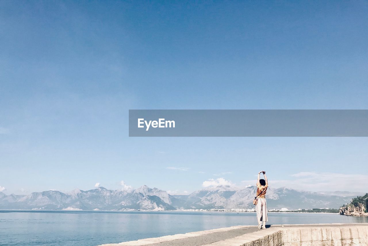 Woman looking at sea against blue sky