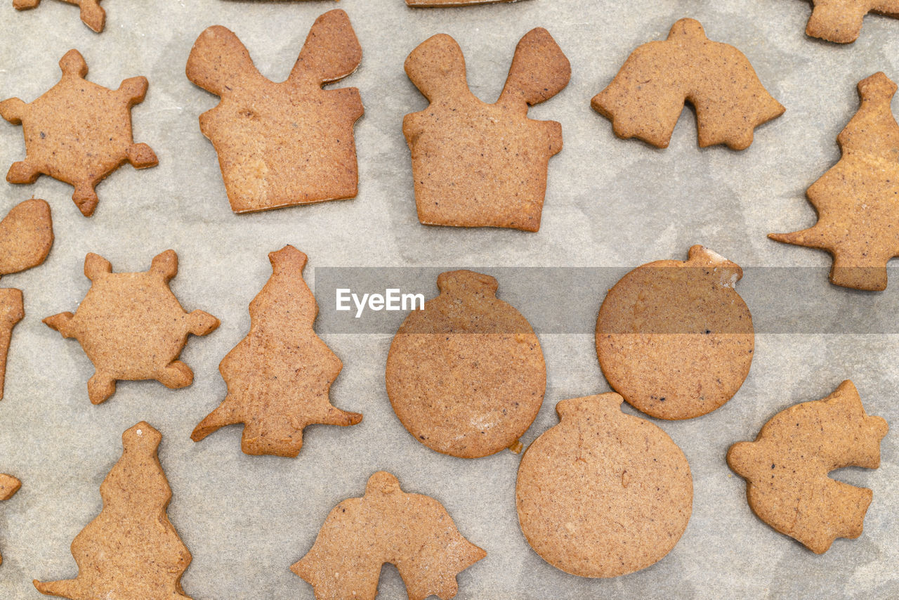 Baked gingerbread cookies in various shapes without decorations, lying on baking paper, top view.