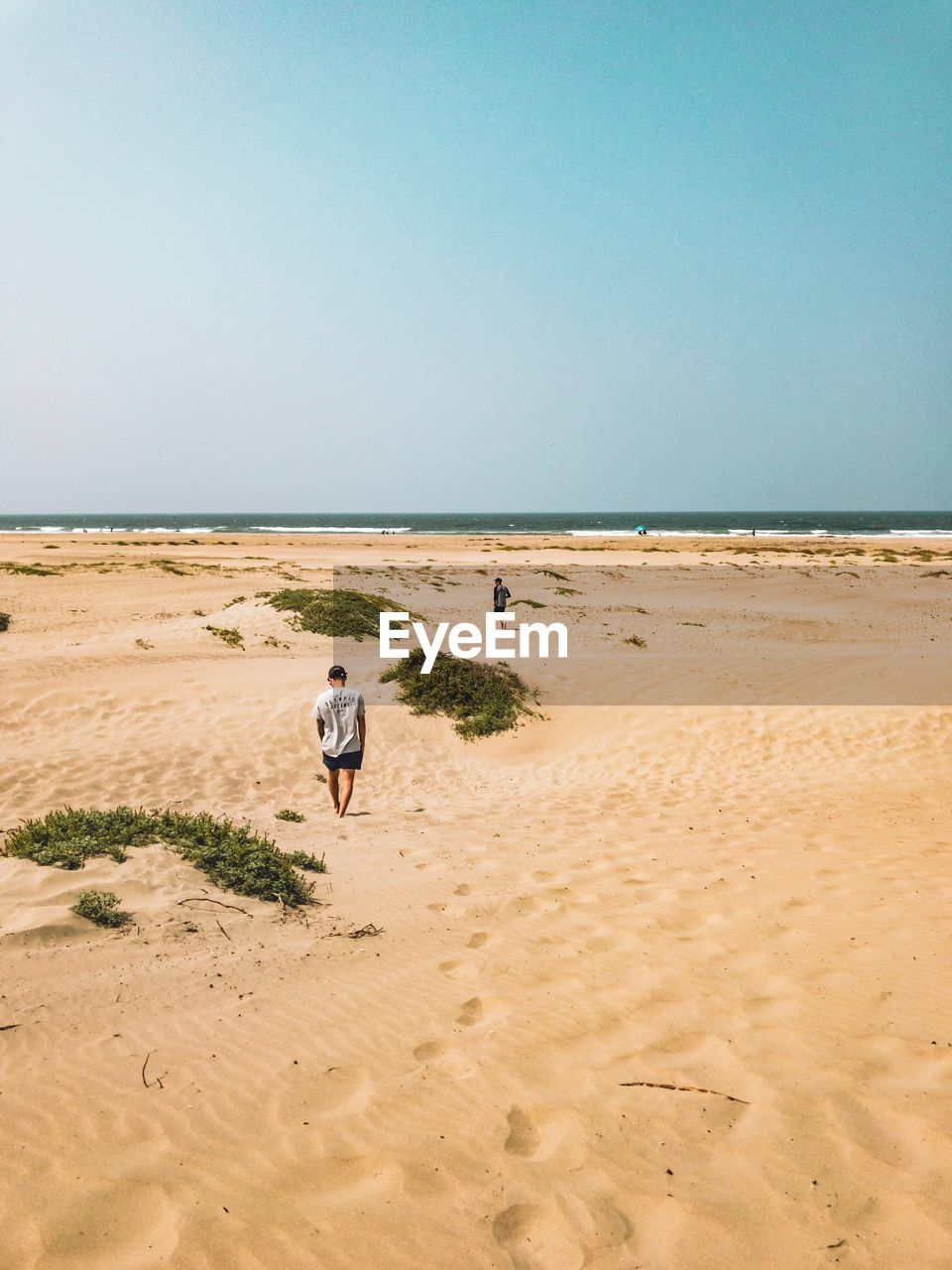 MAN WALKING ON BEACH AGAINST CLEAR SKY