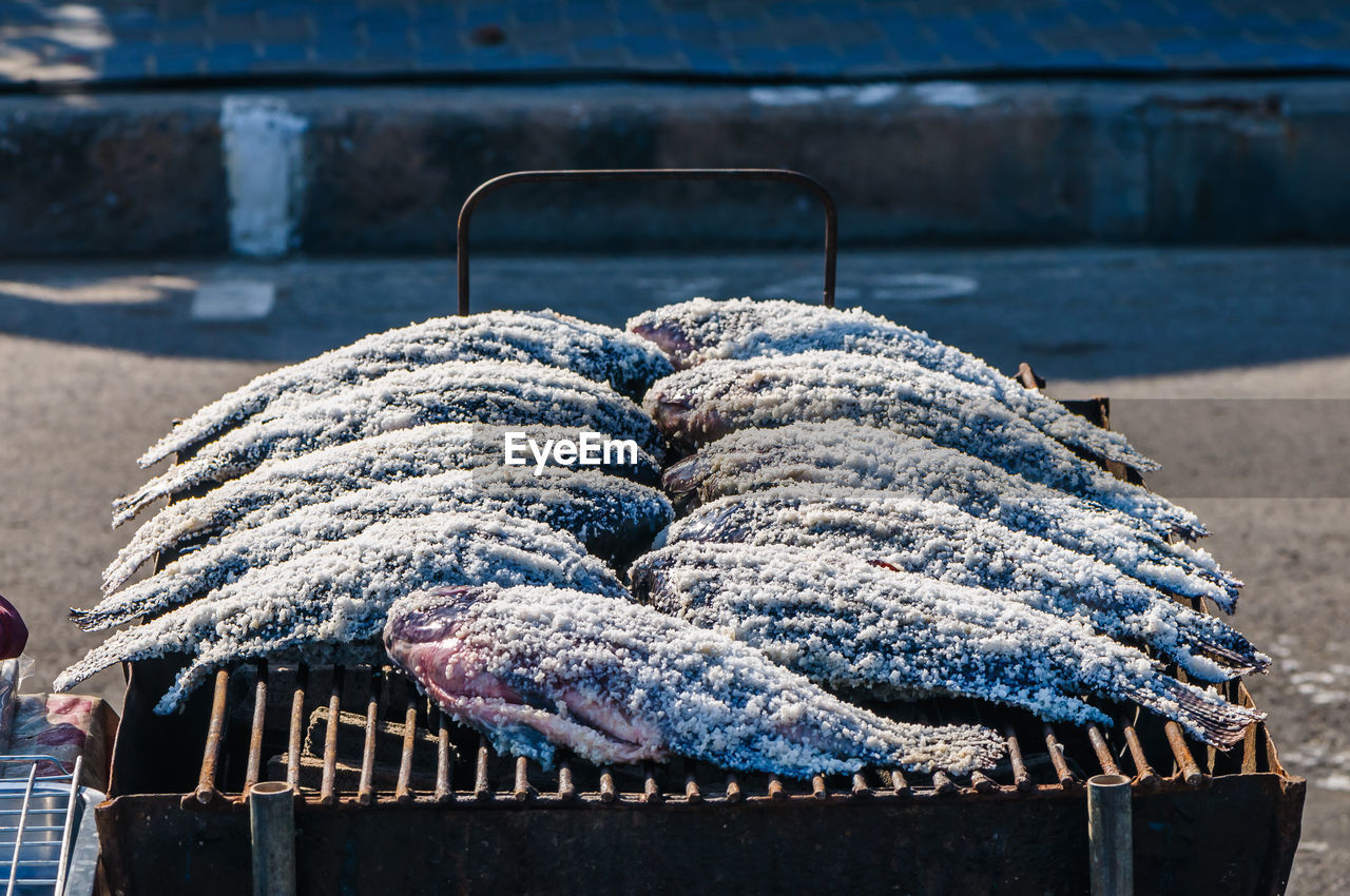 High angle view of fish covered with salt on barbecue at market stall