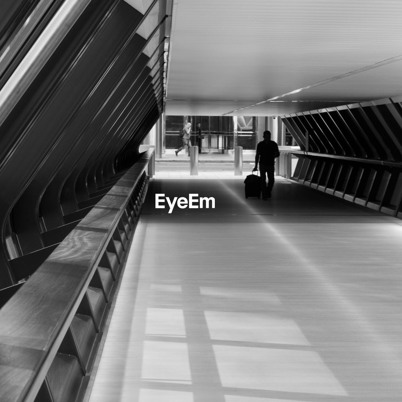 REAR VIEW OF WOMAN WALKING IN ILLUMINATED MODERN CORRIDOR