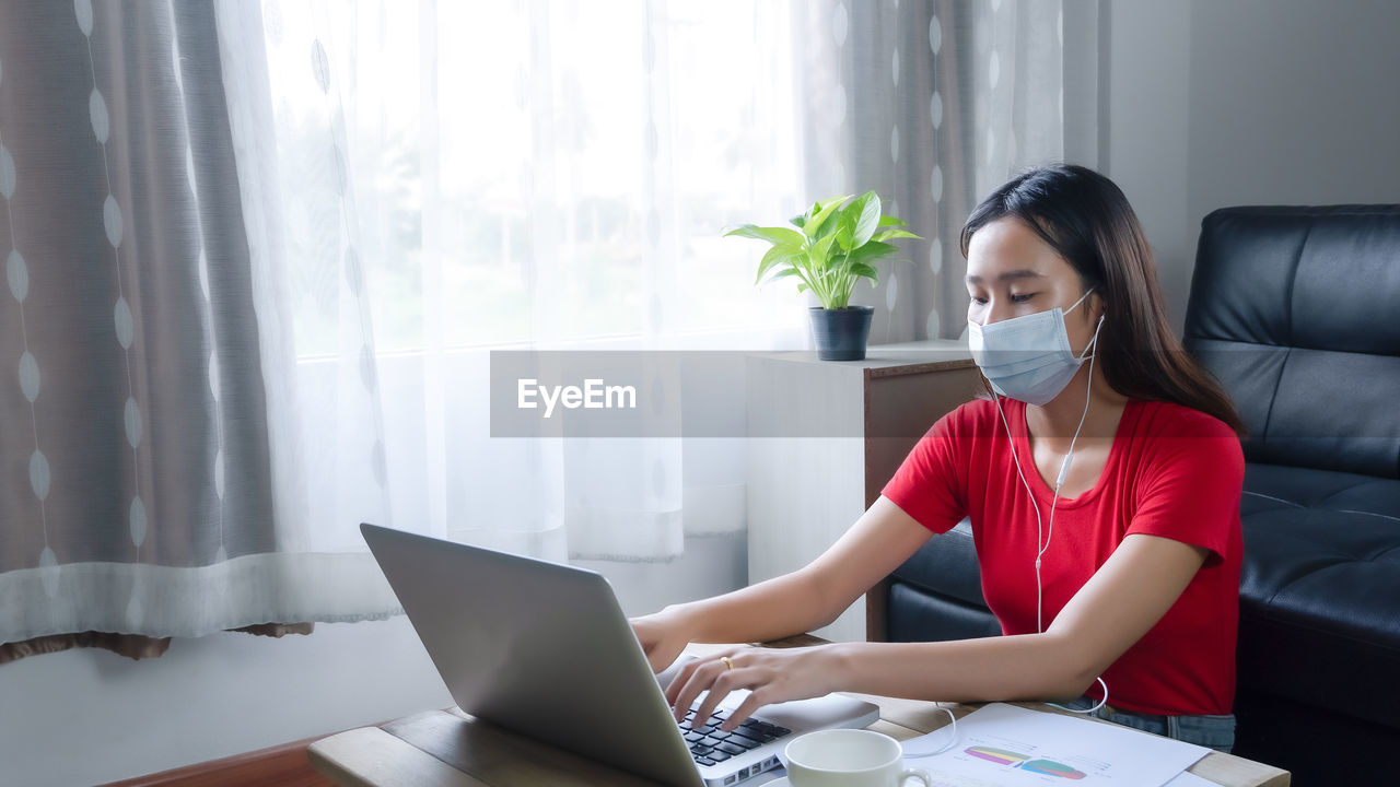 Woman wearing mask using laptop while sitting at home