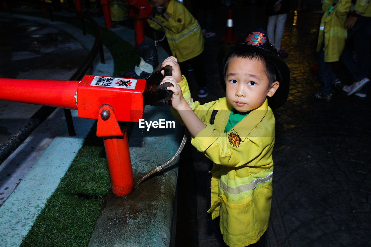 Portrait of boy wearing protective workwear holding machine at fire station