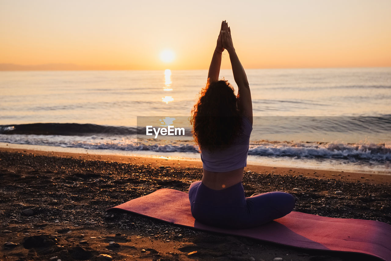 side view of woman standing at beach during sunset