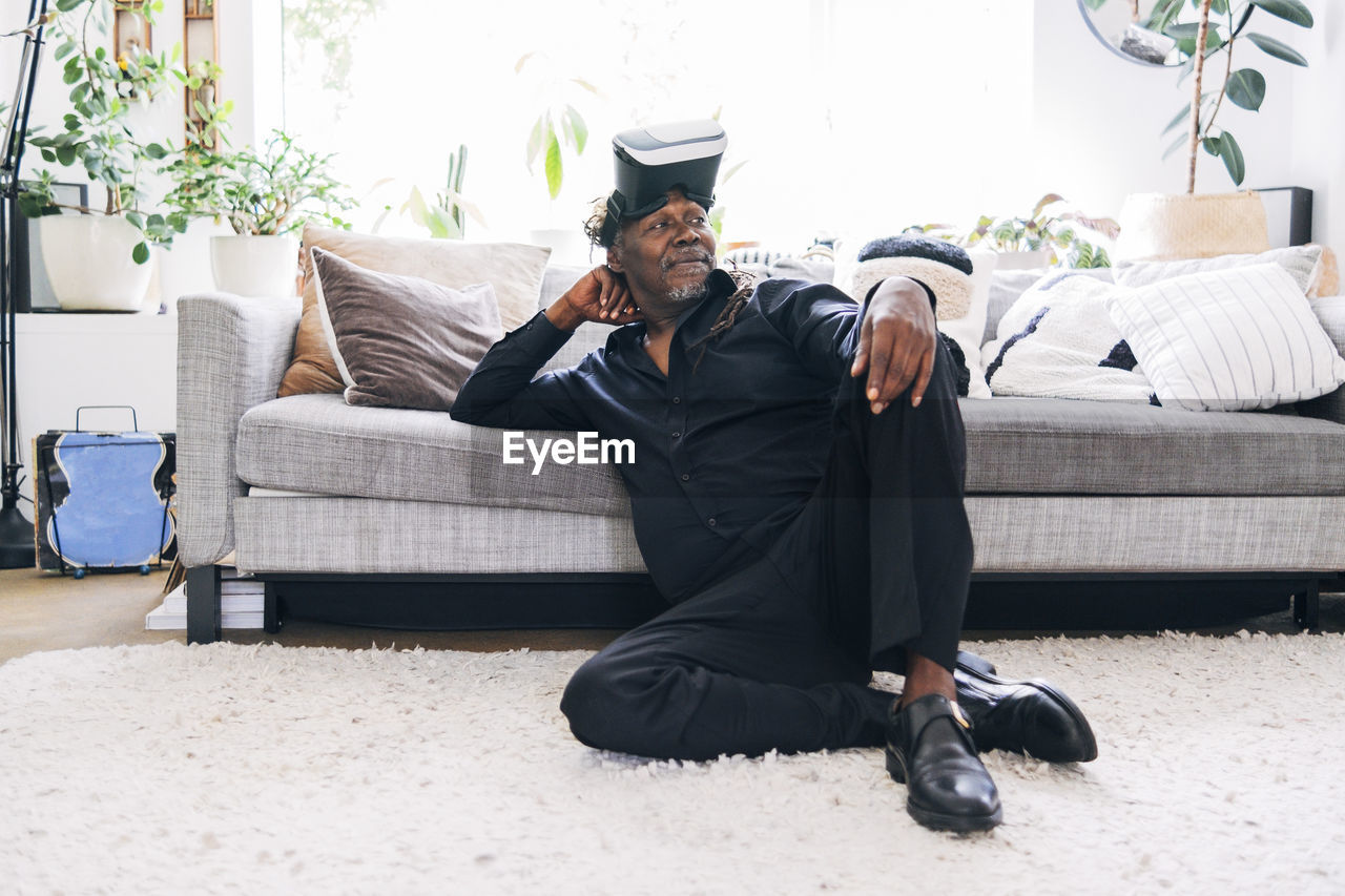 Relaxed man with virtual reality headset looking away while leaning on sofa at home