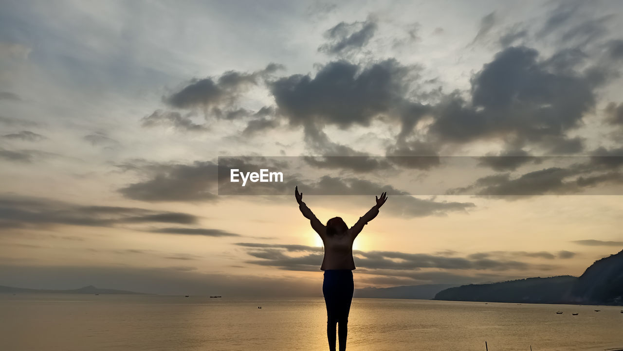 Rear view of silhouette woman standing in sea against sky