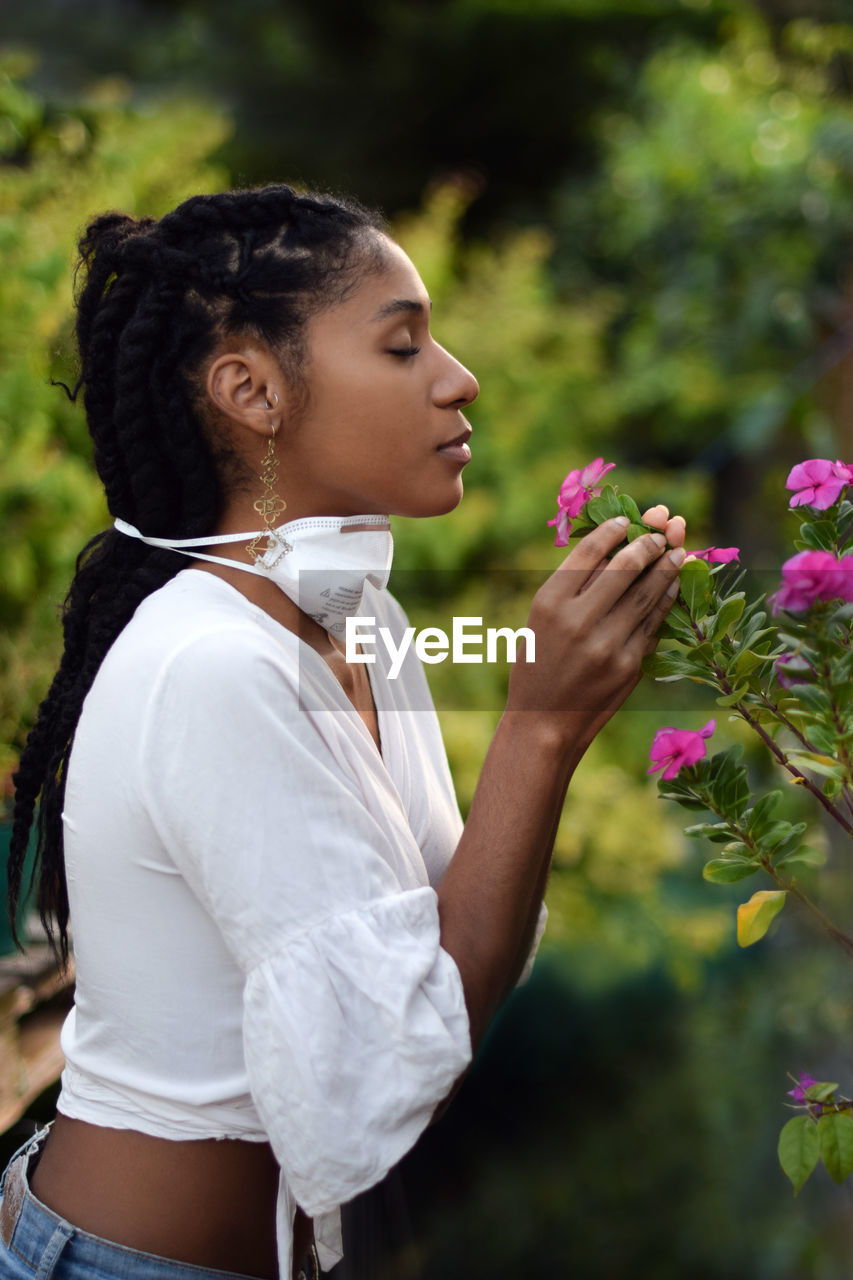 Young woman takes face mask off to smell the flowers