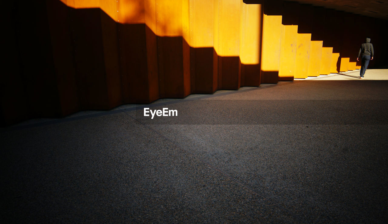 Rear view of man walking by orange wall