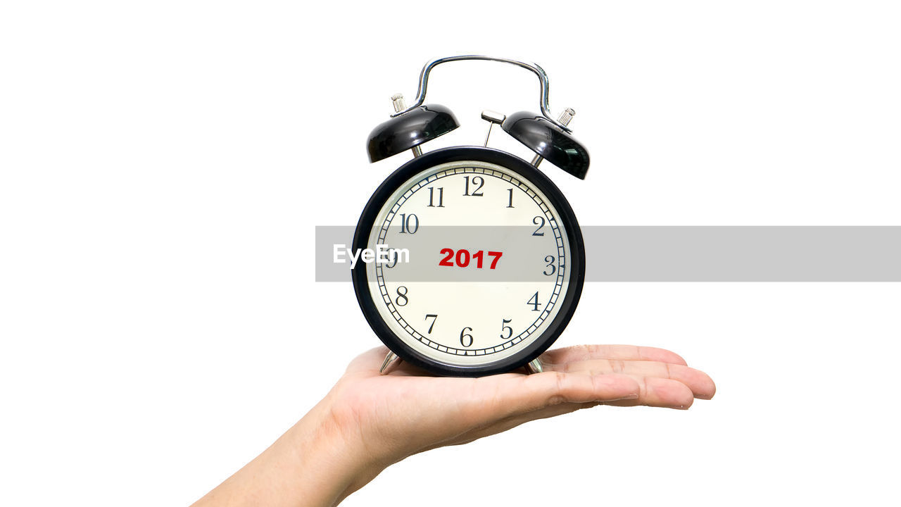 Cropped hand holding alarm clock over white background