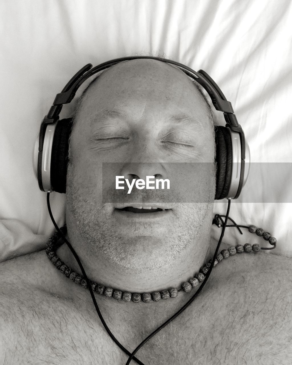 High angle view of shirtless man with eyes closed listening music on bed