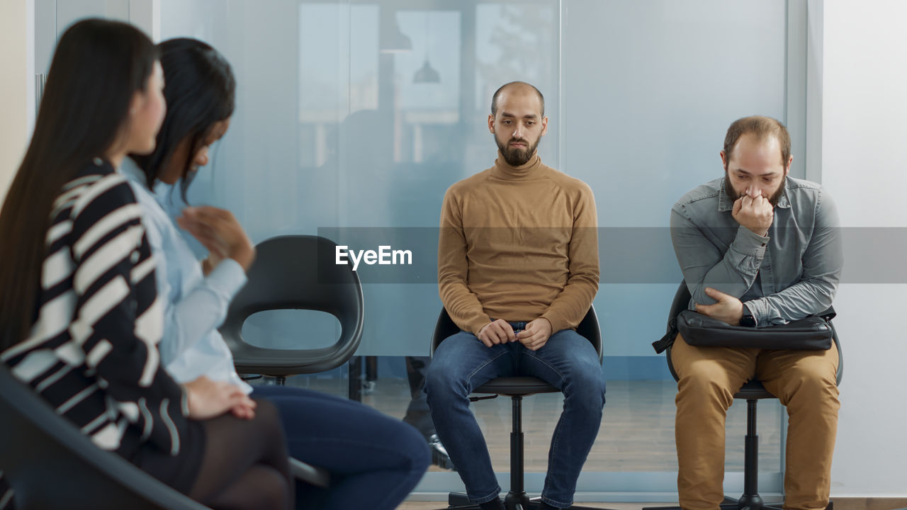 Colleagues sitting together on chair in waiting room