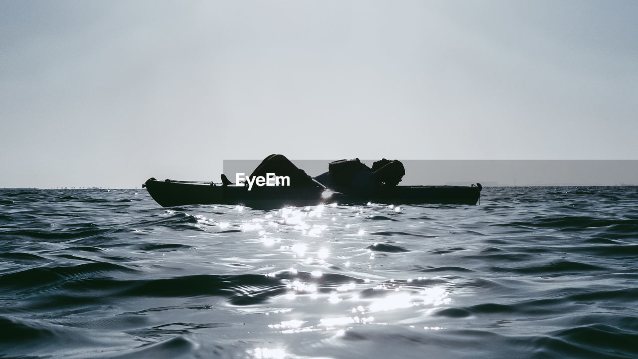 Men floating on sea against clear sky