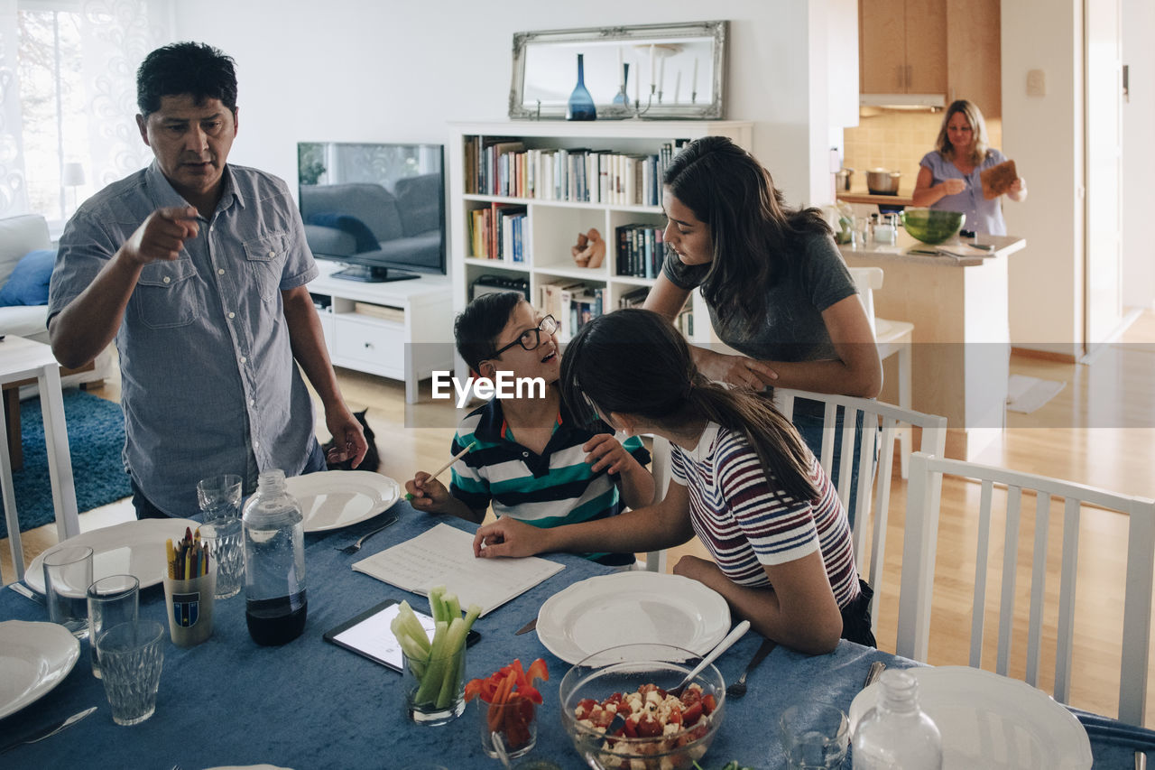 Sisters looking at boy while father standing by dining table