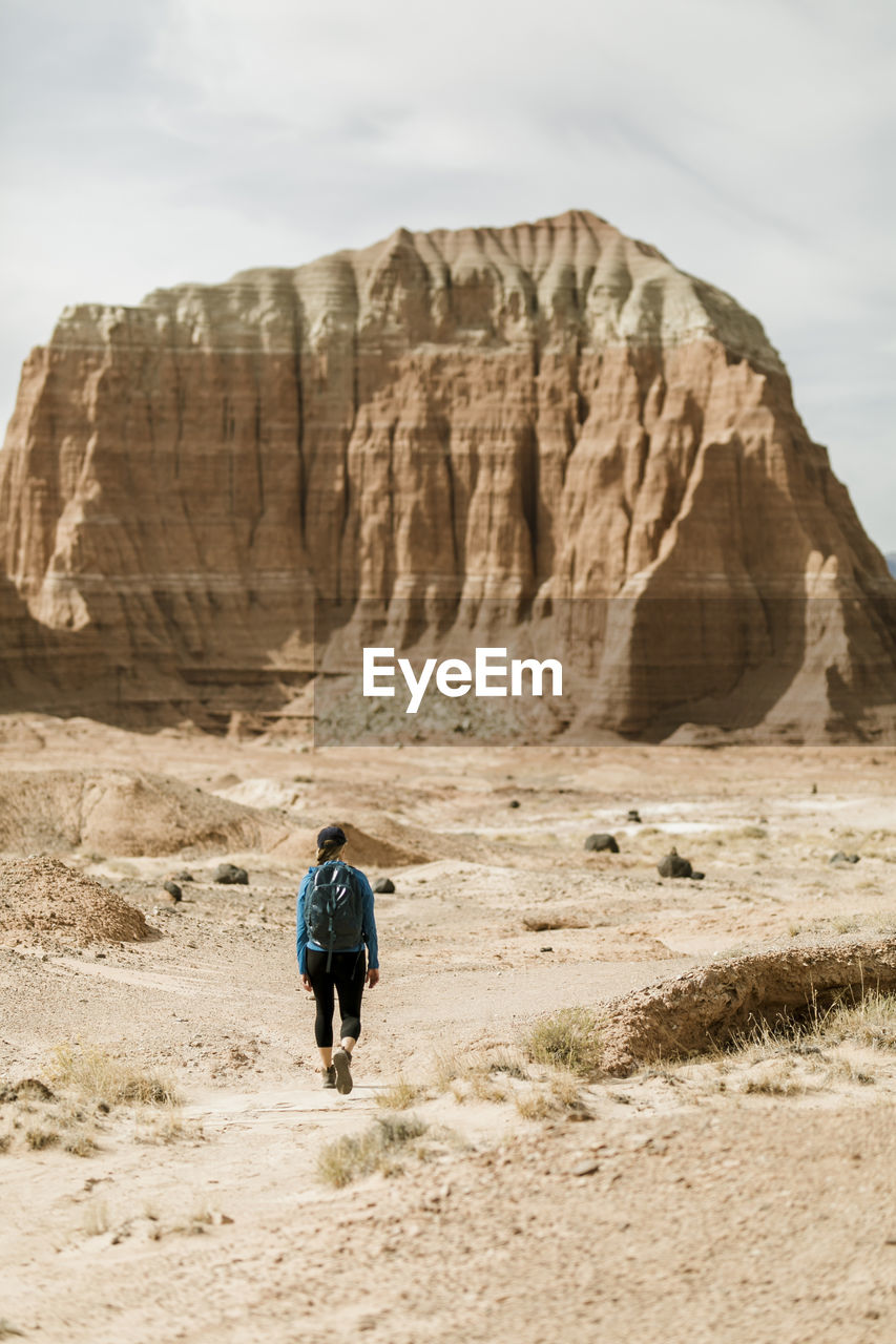 Rear view of female hiker with backpack exploring desert against rock formations during sunny day