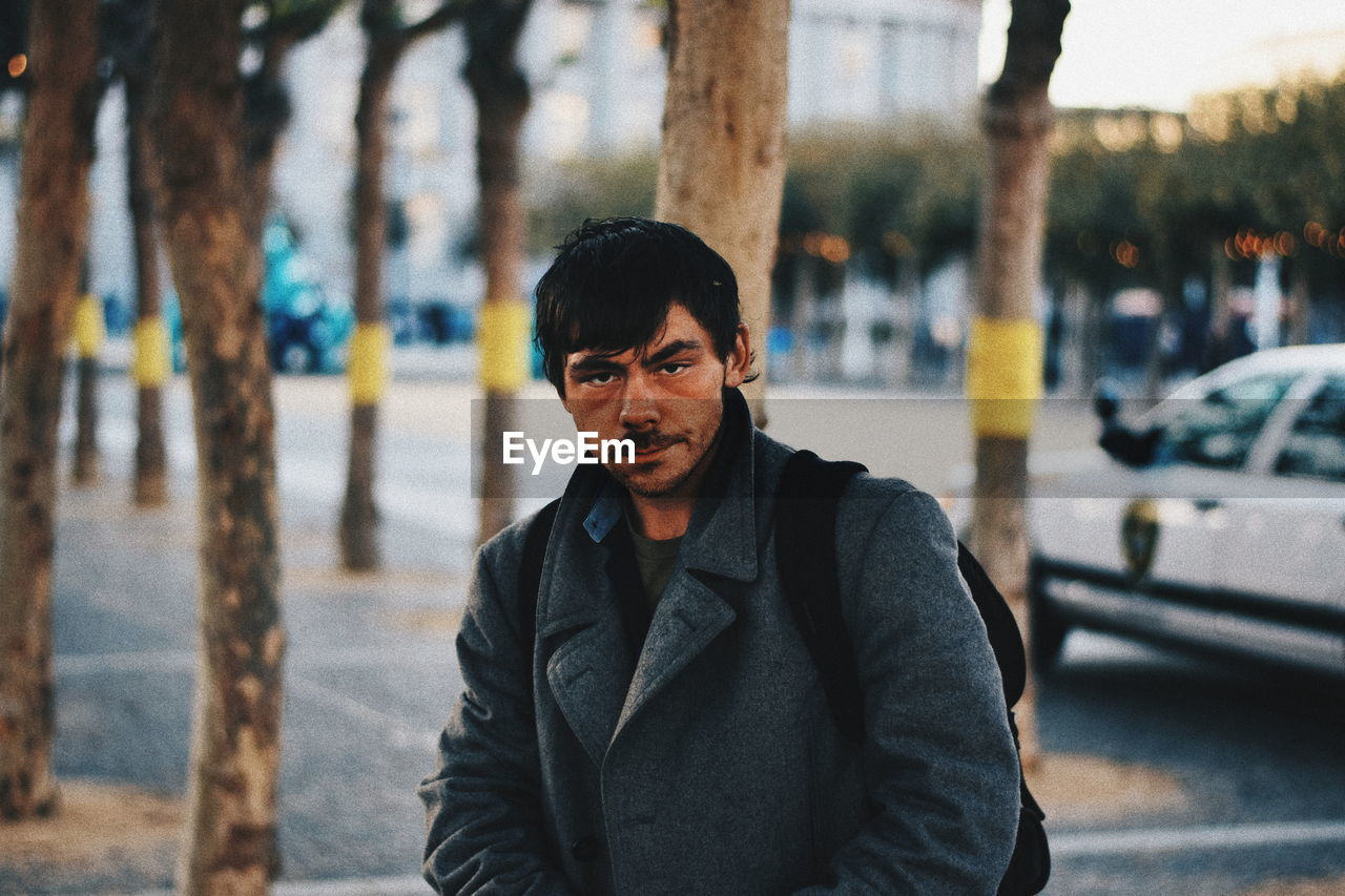 PORTRAIT OF MATURE MAN STANDING AGAINST TREES