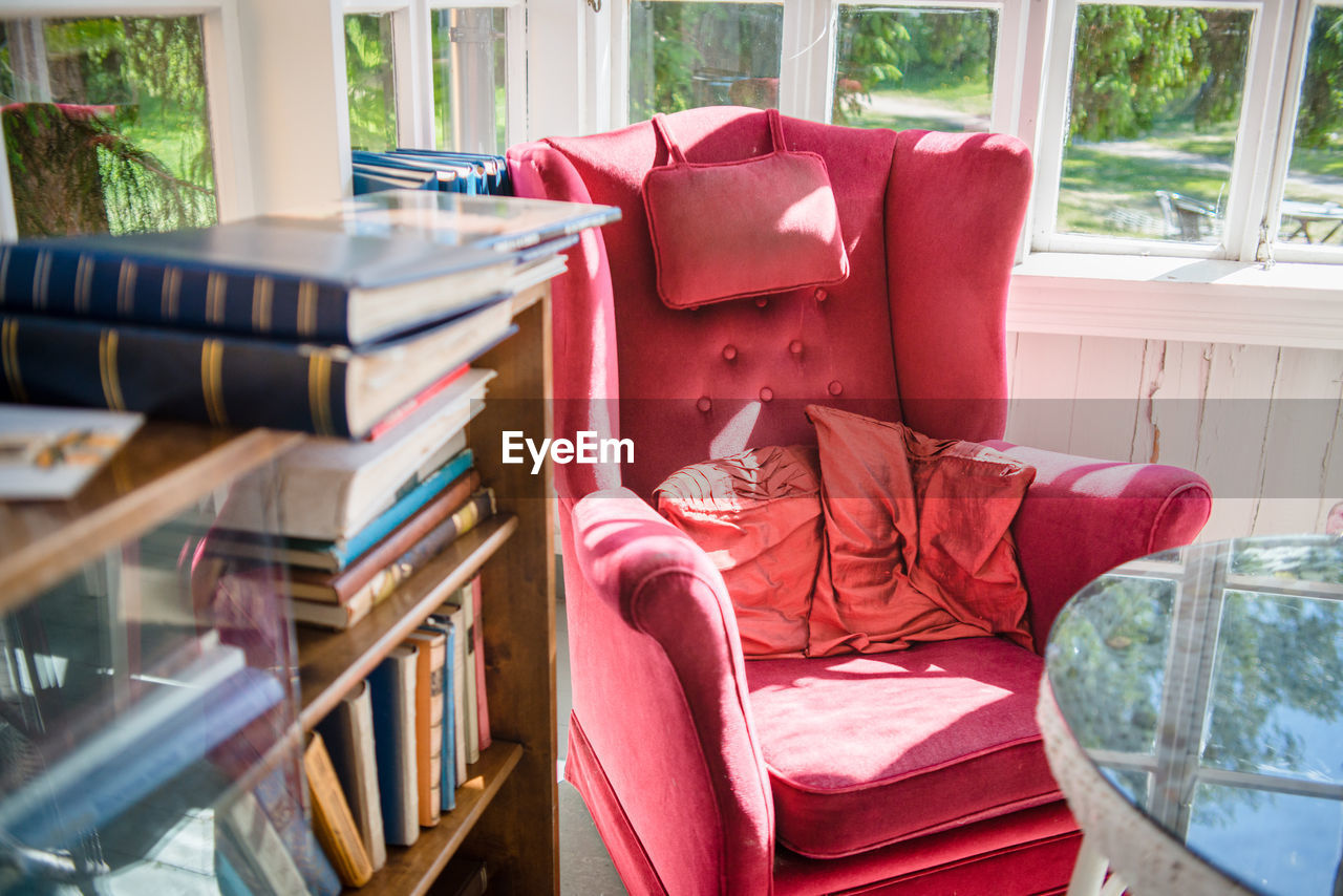 High angle view of red armchair by books rack against window