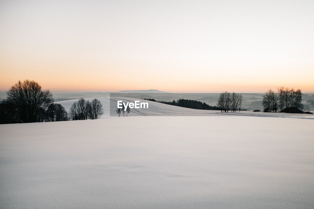 Snow covered field against sky during sunset