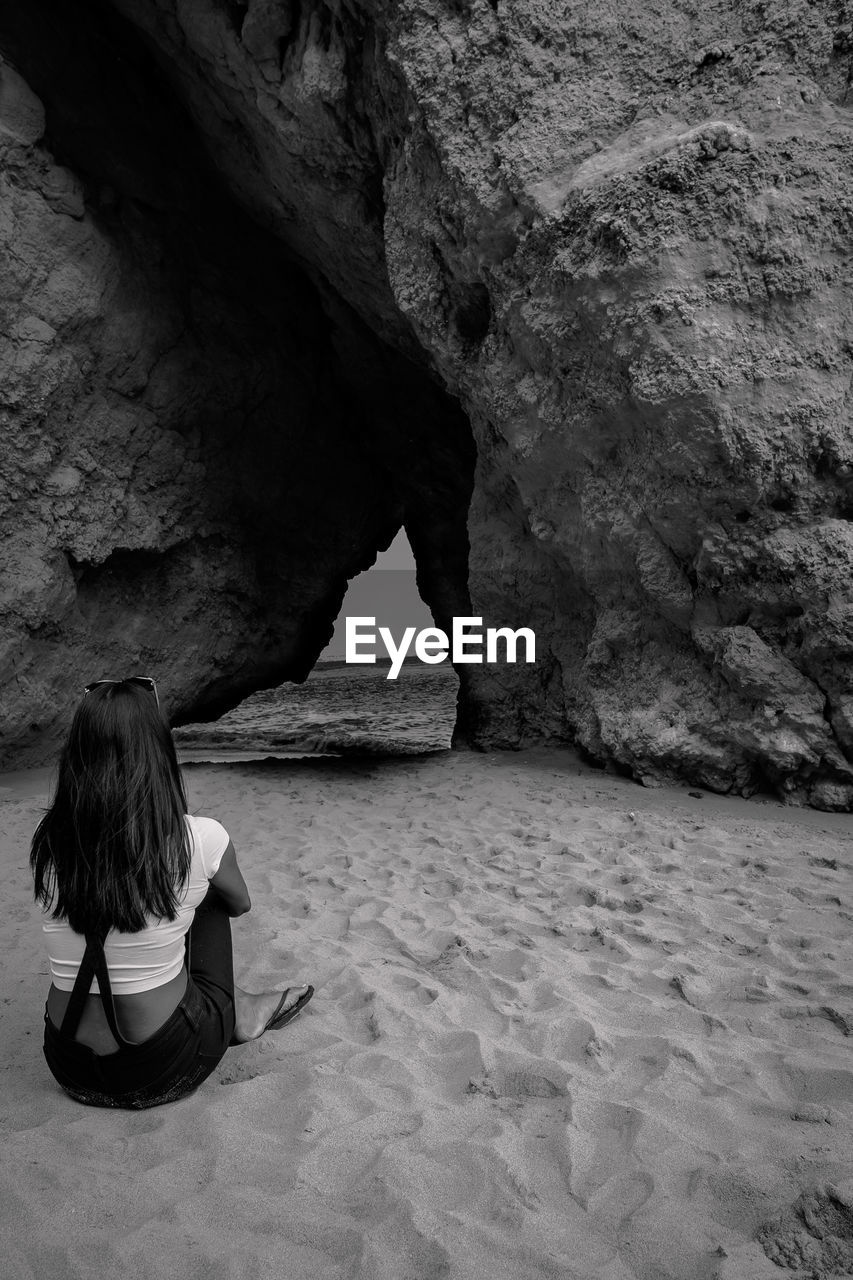 Rear view of woman sitting on sand against rock formation
